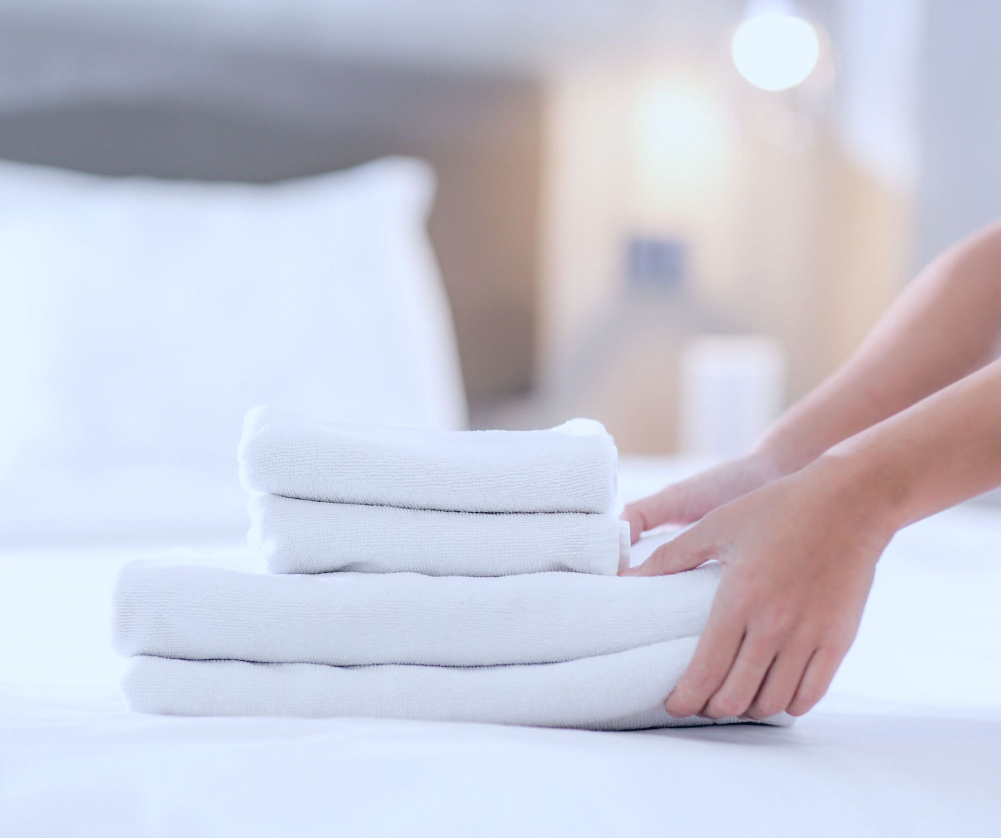 Gestapelte, weiße Handtücher auf einem Bett, eine Hand ordnet sie.