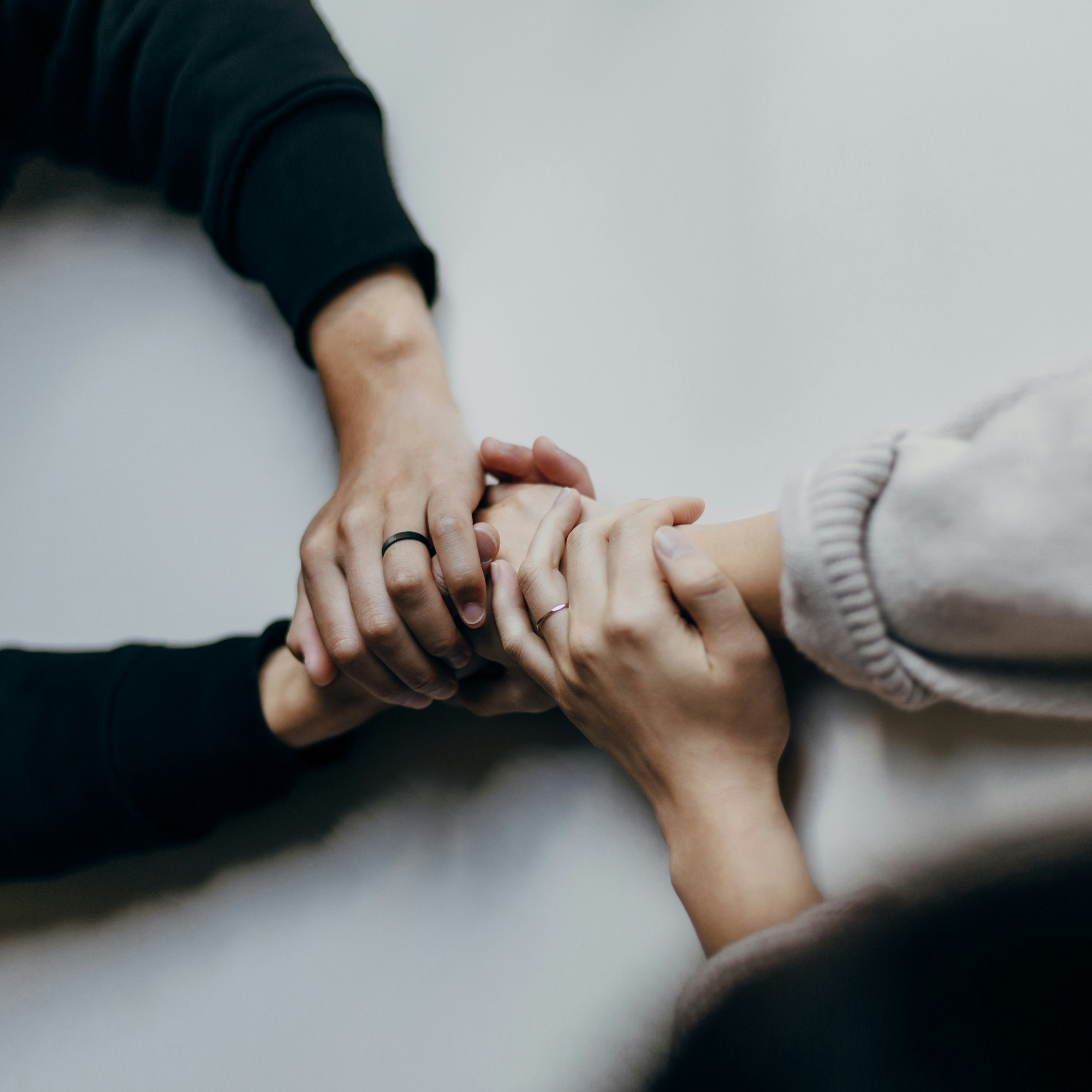Zwei Personen halten sich mit beiden Händen, eine trägt einen schwarzen Ring, die andere einen silbernen Ring.